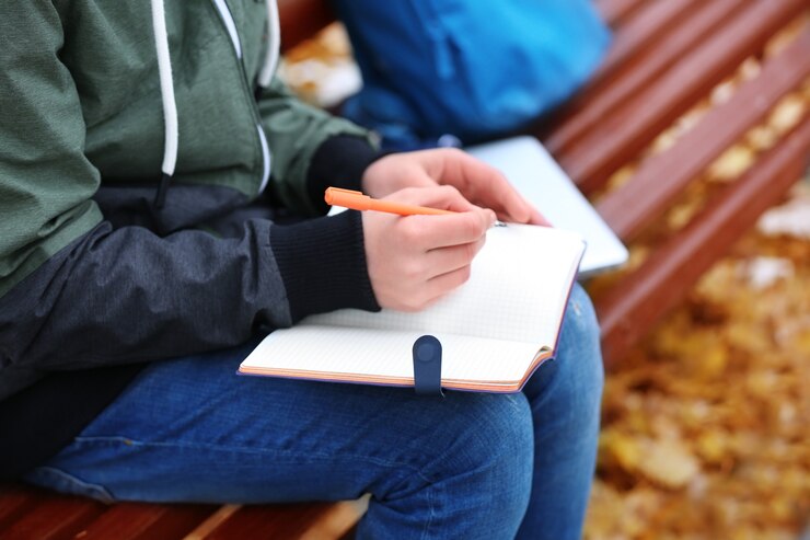 teenager-writing-notebook-while-sitting-bench-autumn-park-close-up_392895-1628